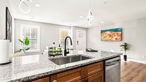 Una cocina moderna con encimeras de granito, un lavamanos de acero inoxidable, armarios de madera y un lavavajillas.
