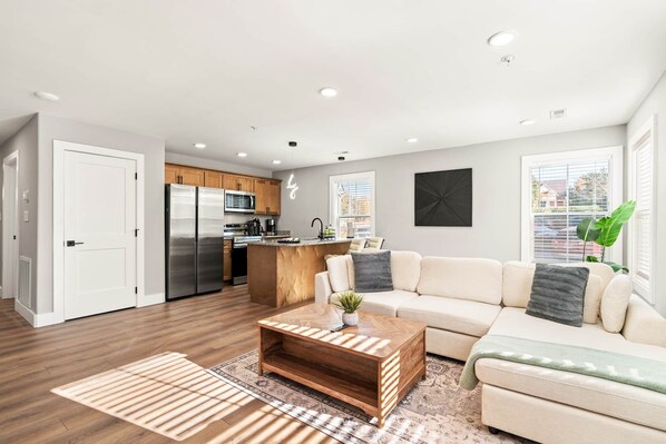 A modern kitchen with stainless steel appliances, a wooden island, and a dining area with a white sofa and a coffee table.