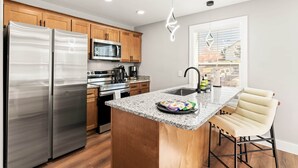 Una cocina moderna con electrodomésticos de acero inoxidable, gabinetes de madera y encimeras de granito, además de una zona de bar con taburetes.