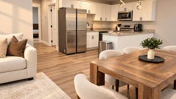 A modern kitchen with stainless steel appliances, a dining area with a wooden table, and a living room with a sofa.