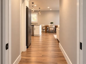 A hallway leading to a kitchen and dining area with wooden flooring and pendant lighting. - The Neyland Nest D (On UTK campus, free parking) (Knoxville)