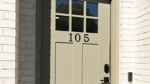 Eine beigefarbene Tür mit der Nummer 105, ein kleines Fenster und ein Klingel.