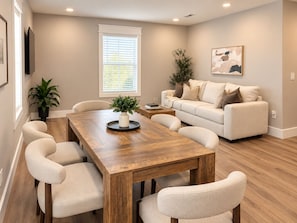 A modern living room with a wooden dining table, beige sofa, and a painting on the wall. - The Neyland Nest D (On UTK campus, free parking) (Knoxville)