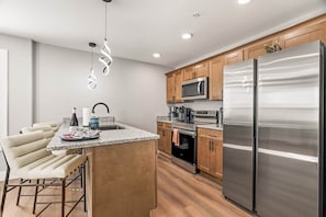 Una cocina moderna con gabinetes de madera, electrodomésticos de acero inoxidable y una zona de bar con taburetes.