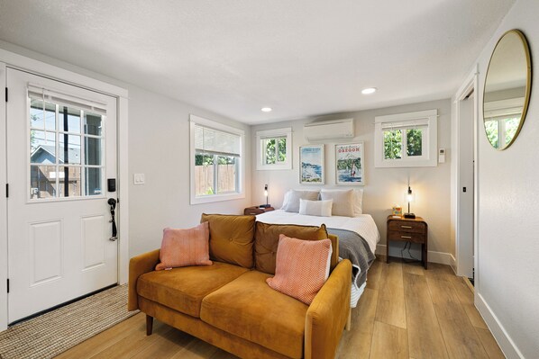 A bedroom with a bed, a brown sofa, a nightstand, and a mirror.
