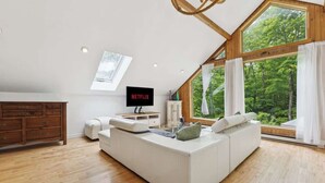 Une chambre de style loft moderne, dotée d’une grande lucarne, d’un canapé blanc, d’un téléviseur et d’une commode en bois.