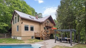 Une maison en bois à deux étages, dotée d’une terrasse, d’une piscine et d’un espace extérieur aménagé et couvert.