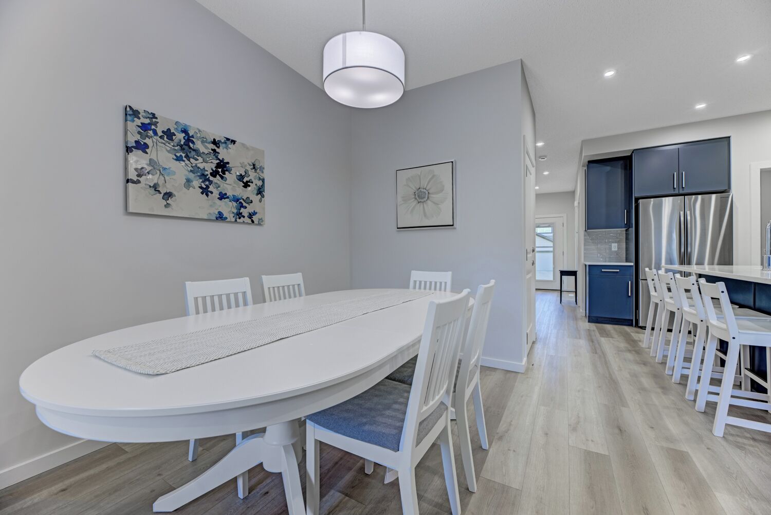 Eine moderne Küche mit einem weißen Esstisch und Stühlen, einem Edelstahlkühlschrank und einem blauen Schrank.