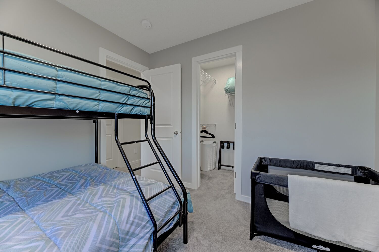 Habitación con literas, una litera inferior y una cama individual, una mesita con una toalla y un armario con perchas.