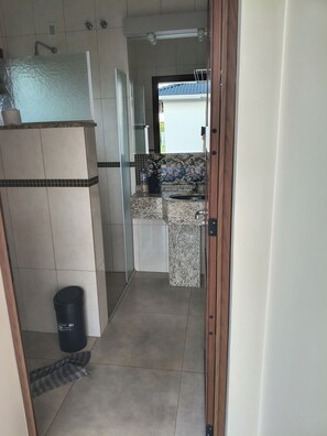 Un pasillo estrecho que lleva a un baño con ducha, lavabo y suelo de baldosas.