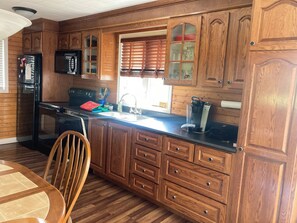 Una cocina con armarios de madera, un refrigerador negro, un lavamanos y una ventana con persianas.