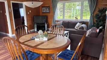 Ein gemütliches Wohnzimmer mit einem Holzesstisch, Stühlen, einer Couch und einem Fernseher.