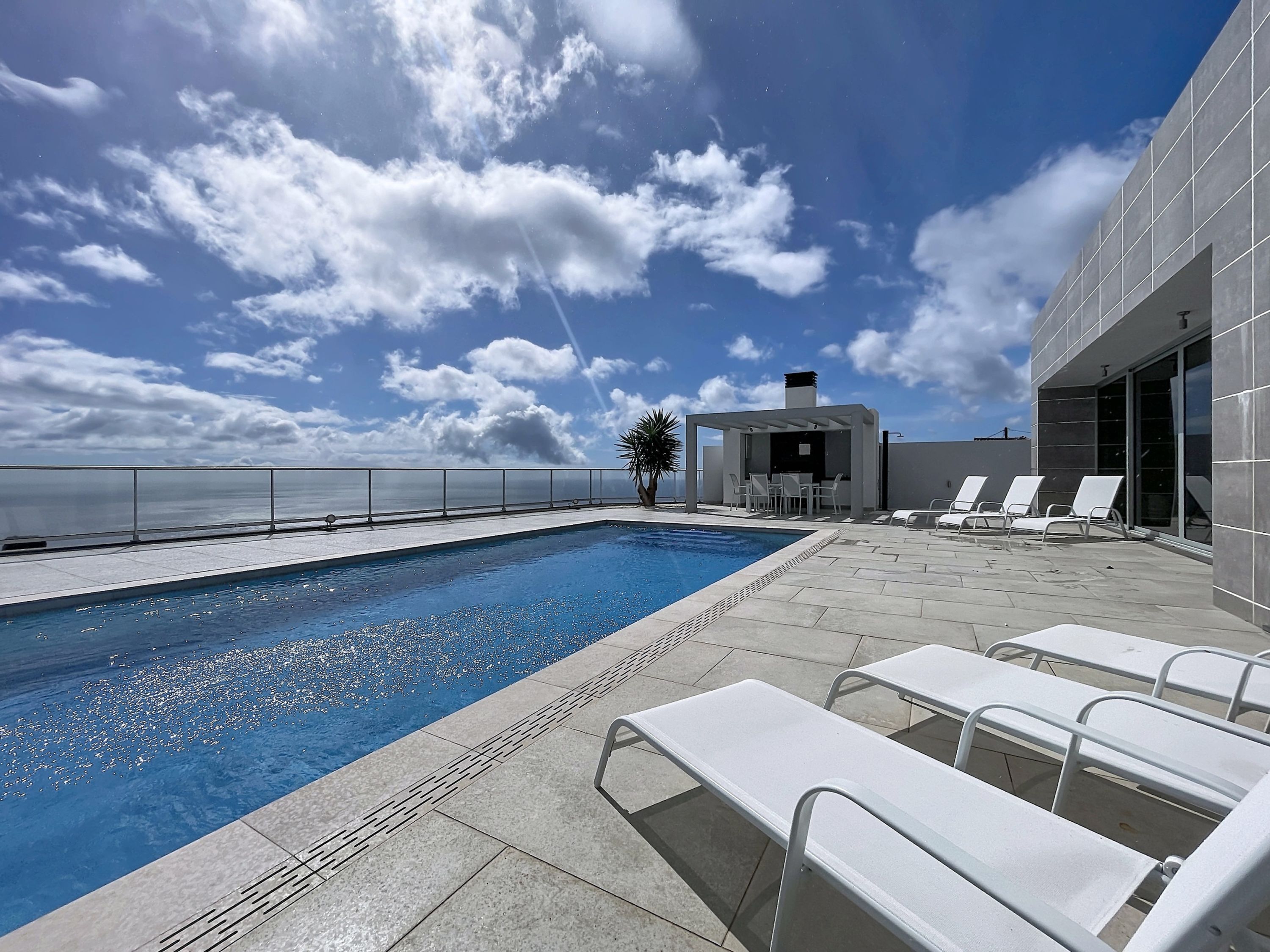 A rooftop pool area with a clear view of the ocean, a covered seating area, and lounge chairs.
