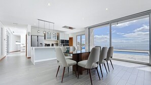 A modern kitchen with a central island, dining area with chairs, and a large window with a view of the sea. - Villa Vista Atl Ntica by Atlantic Holiday (Ribeira Brava)