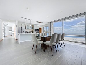 A modern kitchen with a central island, dining area with chairs, and a large window with a view of the sea. - Villa Vista Atl Ntica by Atlantic Holiday (Ribeira Brava)