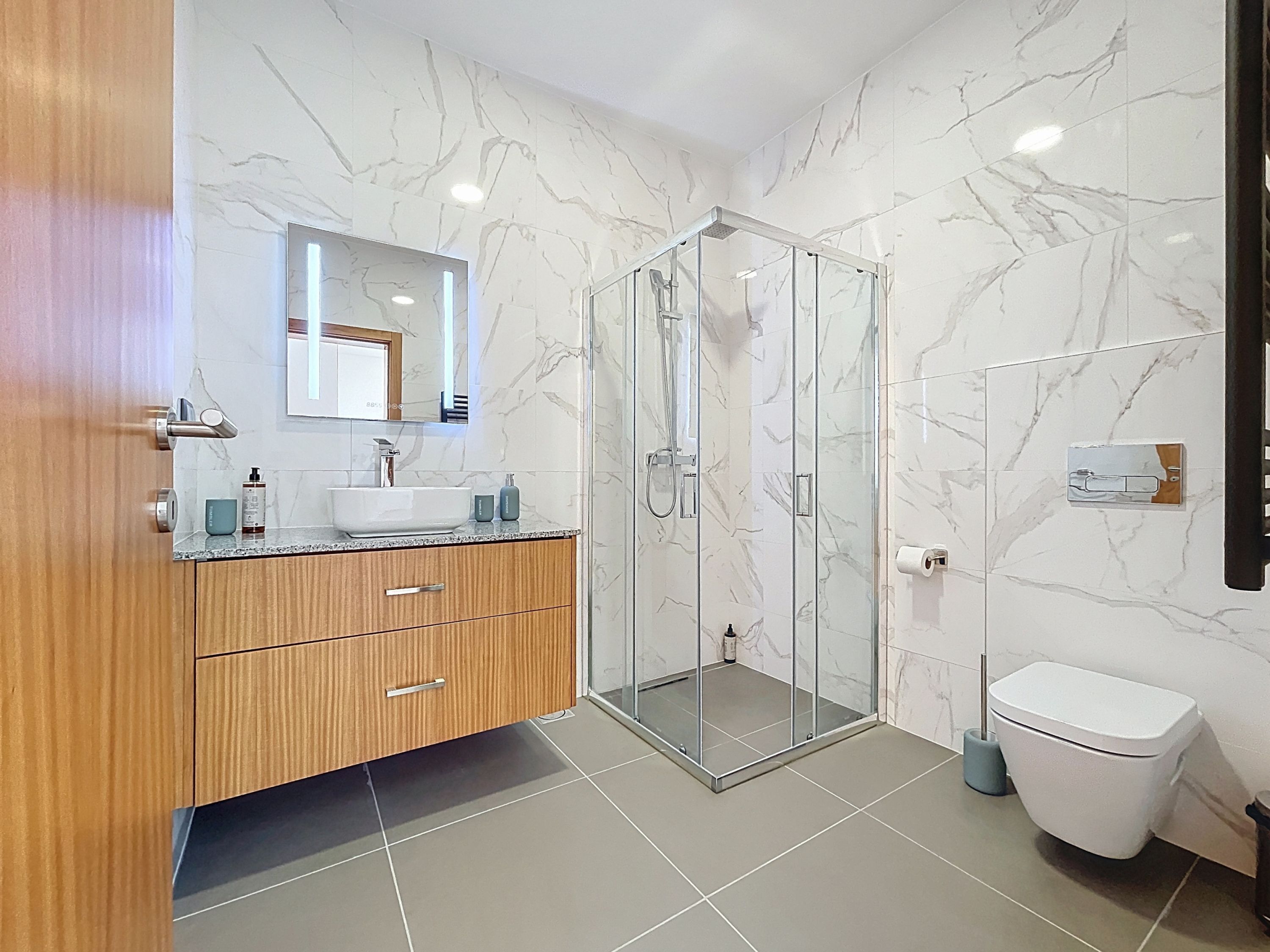 Un bagno moderno con doccia vetrata, mobile lavabo in legno e un water.