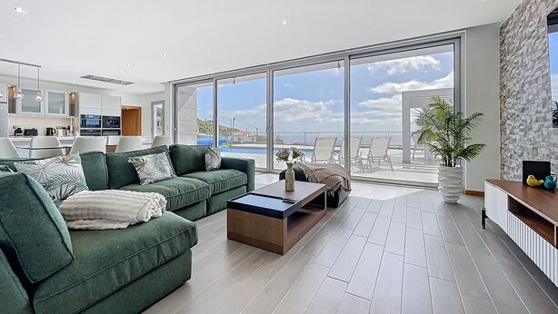 A modern living room with a green sofa, a coffee table, and a view of the sea through large sliding doors. - Villa Vista Atl Ntica by Atlantic Holiday (Ribeira Brava)