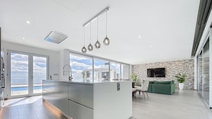 A modern kitchen with a large island, a dining area with a green sofa, and a stone wall with a TV. - Villa Vista Atl Ntica by Atlantic Holiday (Ribeira Brava)