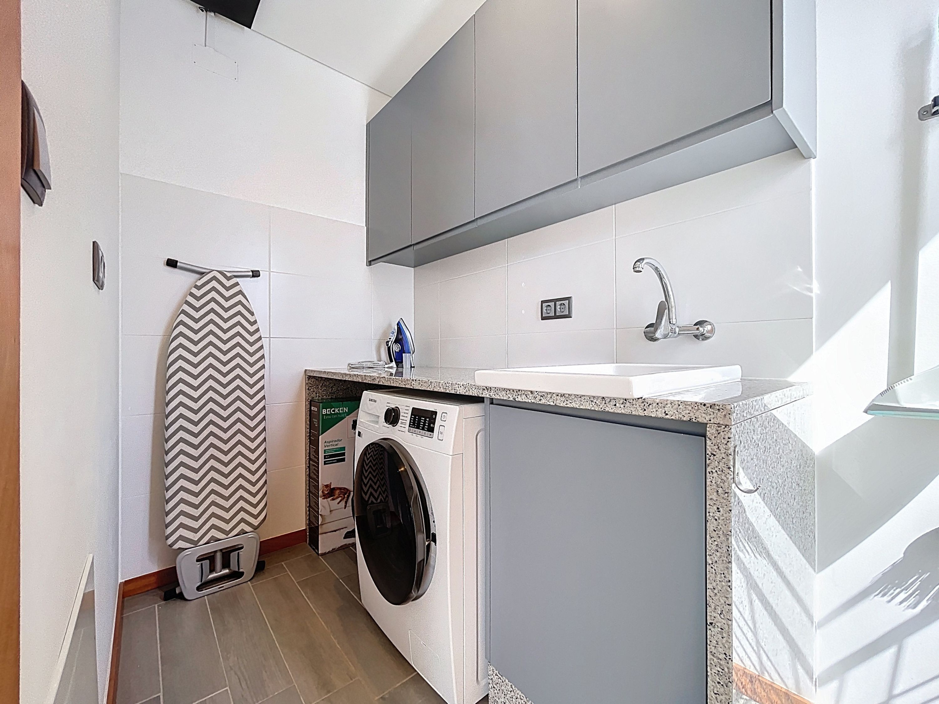 A compact laundry room with a washing machine, a drying rack, and a sink.