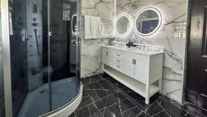 Een moderne badkamer met een douchecabine van glas, een wit wastafelmeubel met marmeren aanrechtblad en een vloer van zwarte tegels.