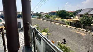 Een balkon met uitzicht op een woonstraat, een heldere lucht en wat groen.