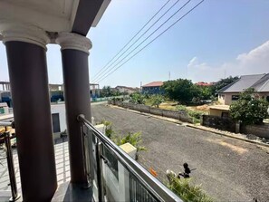 Un balcon donnant sur une rue résidentielle, avec une vue sur un ciel dégagé et quelques espaces verts.
