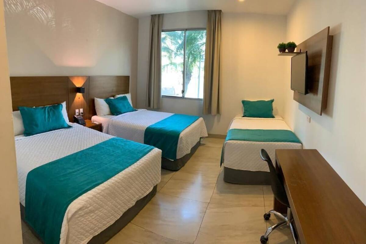 Une chambre d’hôtel avec deux lits, un bureau, une télévision et une fenêtre avec des rideaux.