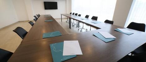 Un salón de conferencias con una larga mesa, sillas y un televisor de pantalla plana en la pared.