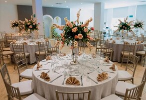 A banquet hall with round tables set for a formal event, each with a floral centerpiece and neatly folded napkins.