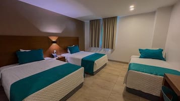 A hotel room with three beds, each with teal bedding and a wooden headboard. There is a nightstand with a lamp and a phone on one side. The room has a tiled floor and a window with curtains.
