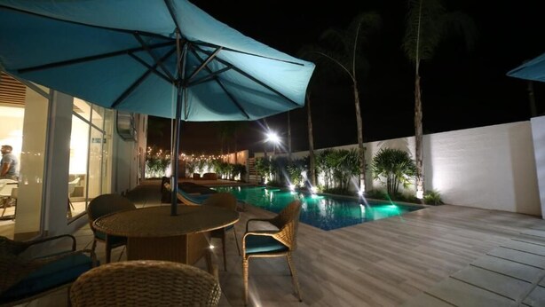 Area piscina all'aperto con tavolo e sedie, circondata da palme e illuminata da luci soffuse.