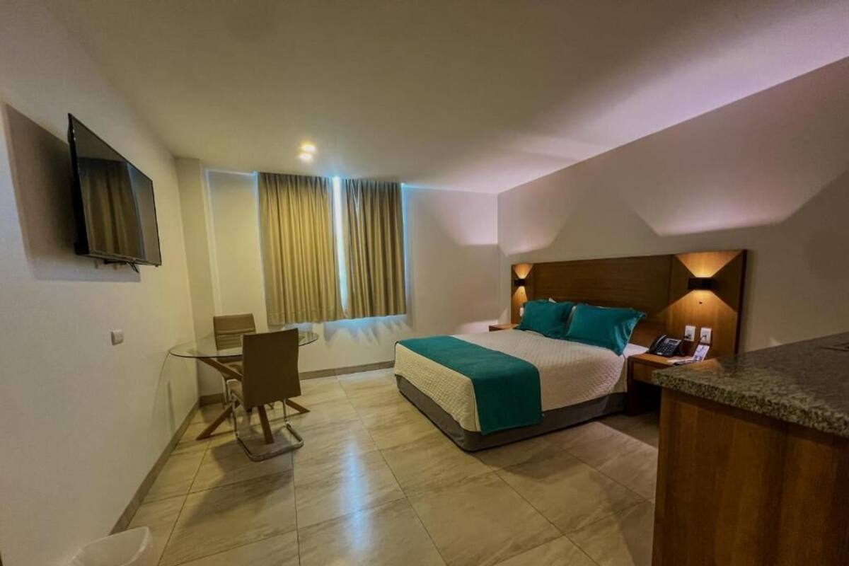 Une chambre d’hôtel équipée d’un lit, d’un bureau, d’une chaise, d’une télévision et d’une petite kitchenette.