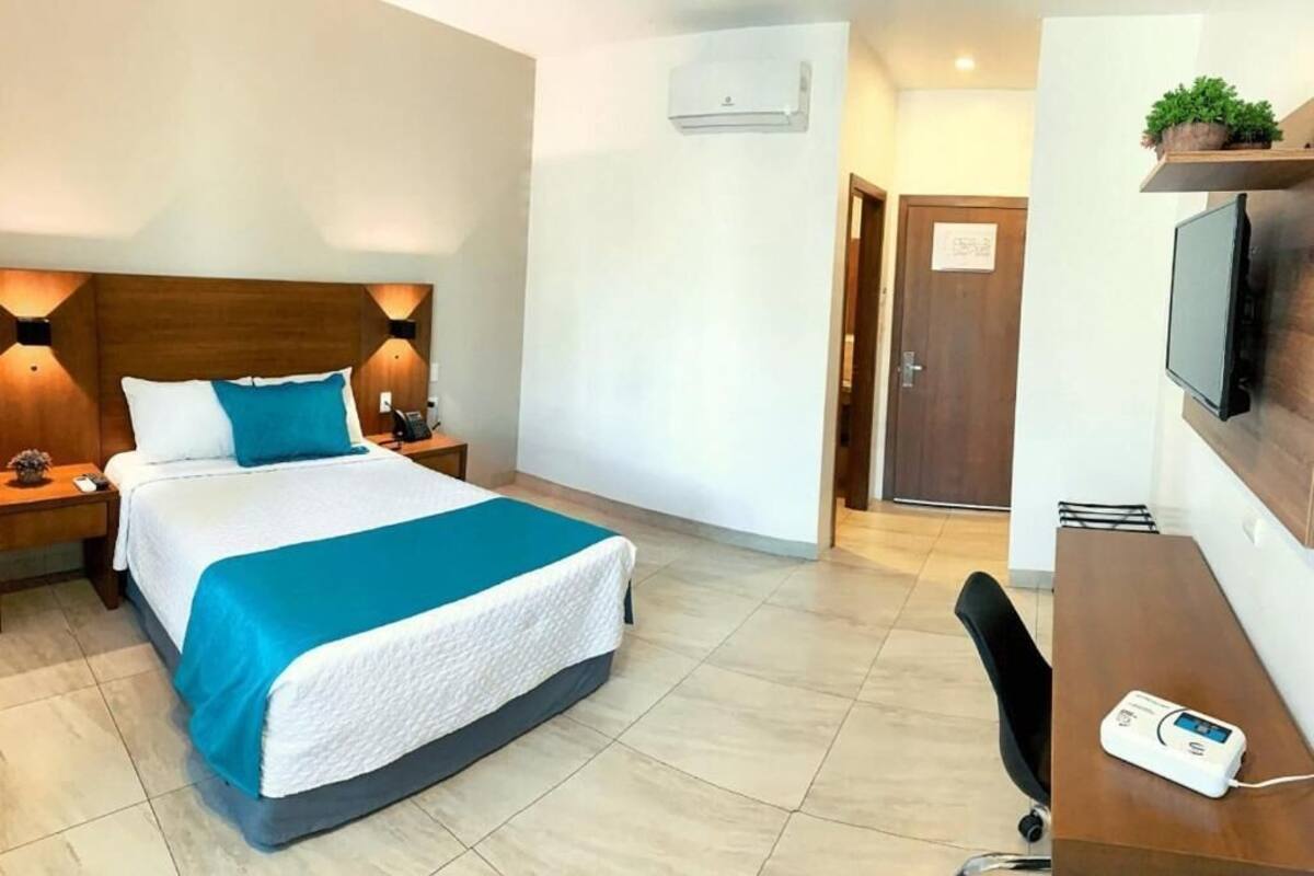 Une chambre d’hôtel équipée d’un lit, de tables de chevet, d’un bureau, d’une chaise, d’un téléviseur et d’un appareil de climatisation.