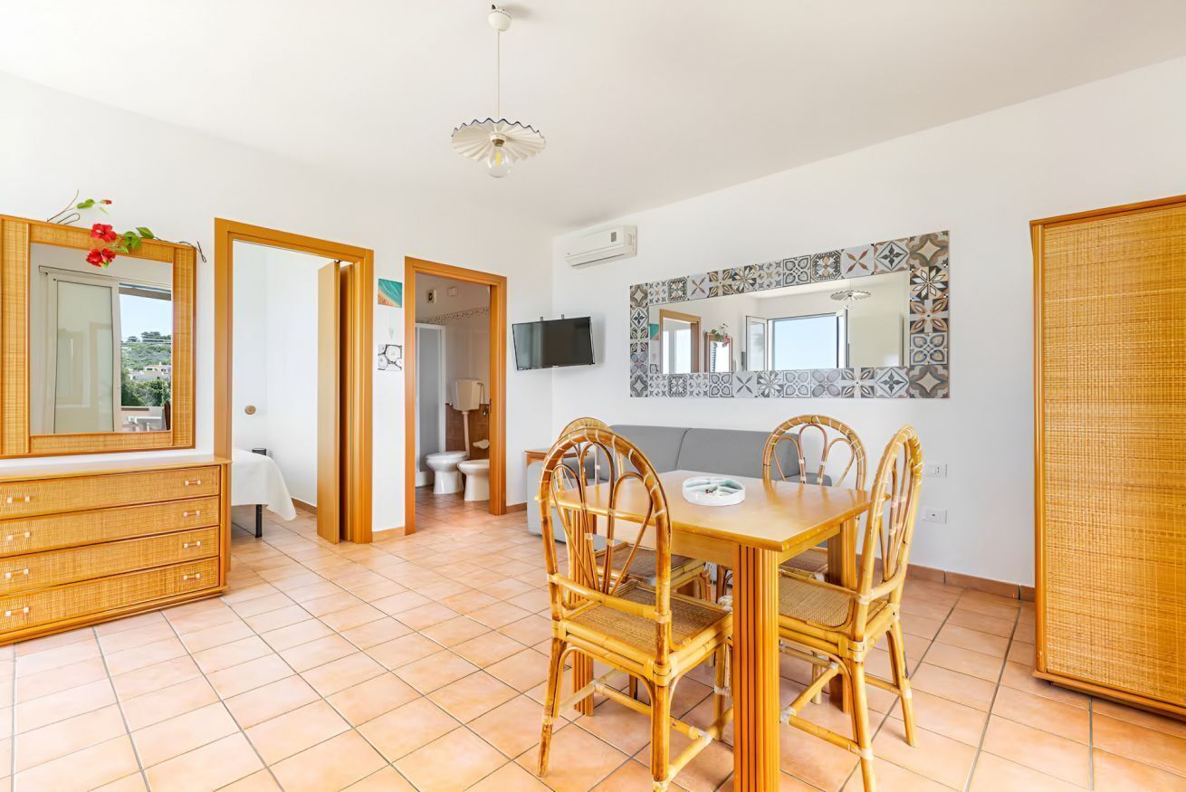 Une pièce comprenant une table à manger, des chaises, un téléviseur et une salle de bain visible à travers une porte ouverte.