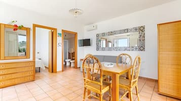 Une pièce comprenant une table à manger, des chaises, un téléviseur et une salle de bain visible à travers une porte ouverte.