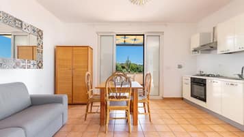 Une cuisine moderne avec des meubles blancs, une table à manger avec des chaises, un canapé gris et une vue à travers une porte vitrée.