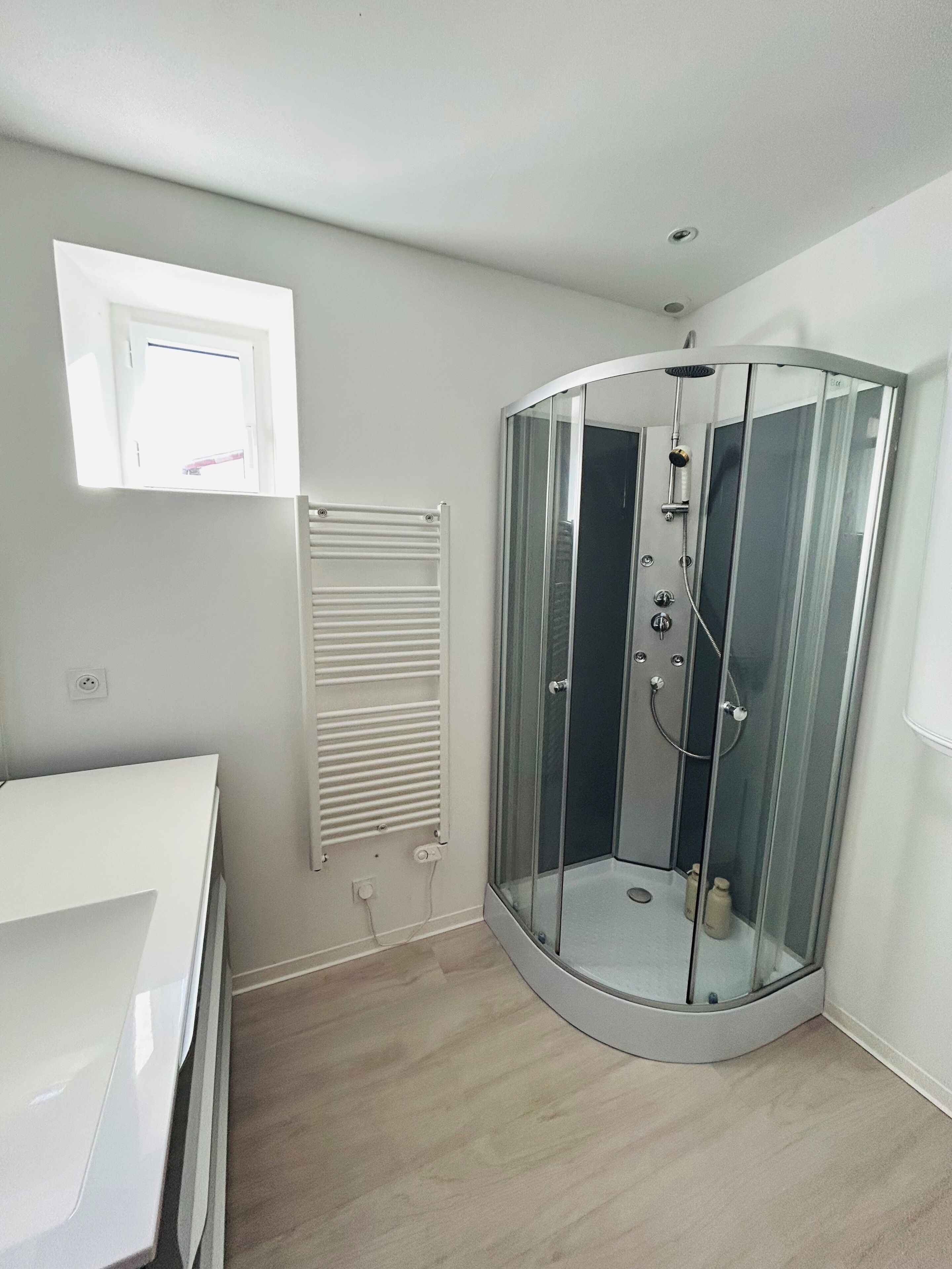 A modern bathroom with a glass-enclosed shower, a white vanity, and a built-in heater.