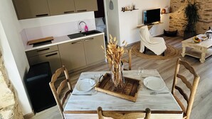 Een moderne keuken met inbouwapparatuur, een eethoek met een marmeren tafel en houten stoelen, en een gezellige zithoek met een stenen muur en een hanglamp.