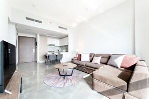 A modern living room with a sofa, coffee table, and a dining area with chairs. - Free Housekeeping Visits During Your Stay - Stayshort - Modern 2BR Retreat in Dubai South for 6 (Dubai)