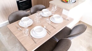 A dining table set with white plates, bowls, and cutlery, surrounded by grey upholstered chairs. - Free Housekeeping Visits During Your Stay - Stayshort - Modern 2BR Retreat in Dubai South for 6 (Dubai)
