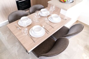 A dining table set with white plates, bowls, and cutlery, surrounded by grey upholstered chairs. - Free Housekeeping Visits During Your Stay - Stayshort - Modern 2BR Retreat in Dubai South for 6 (Dubai)