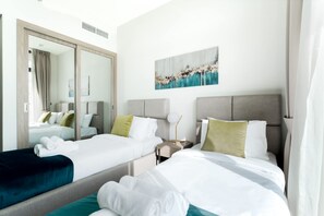 A hotel room with two beds, a large mirror, a painting on the wall, and a nightstand with a lamp. - Free Housekeeping Visits During Your Stay - Stayshort - Modern 2BR Retreat in Dubai South for 6 (Dubai)