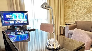 Habitación de hotel con televisor de pantalla plana mostrando Netflix, un escritorio con lámpara, un sofá y una pared con textura de piedra.