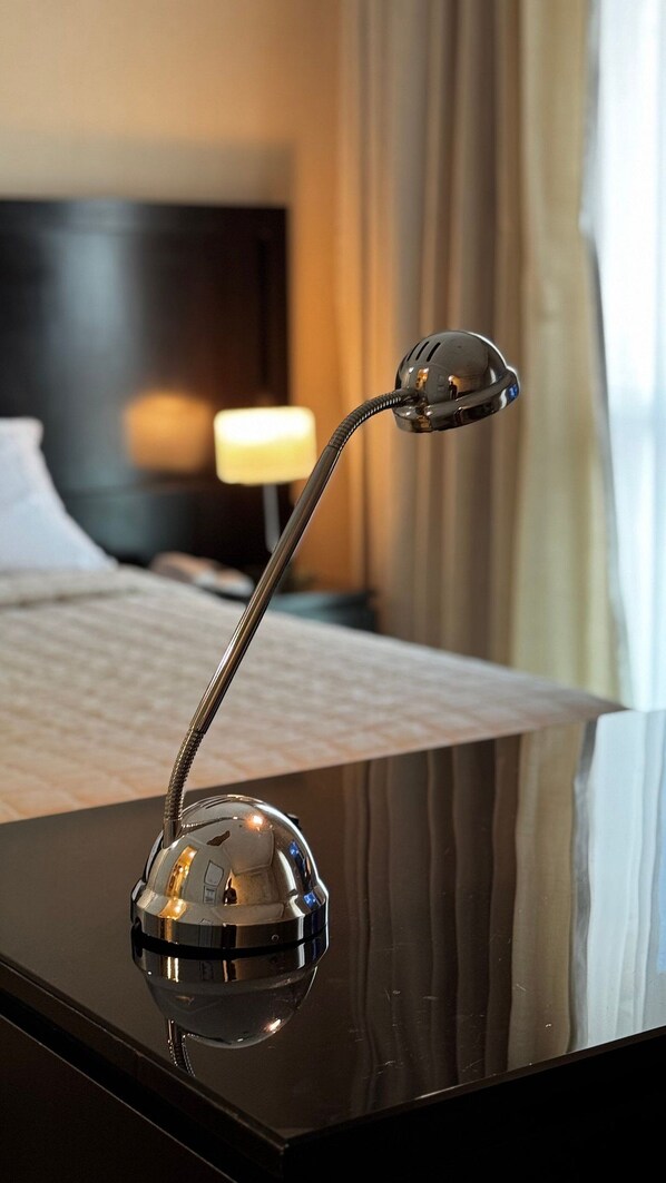 A modern hotel room with a polished black bedside table, a sleek metallic nightstand lamp, and a neatly made bed with white linens. - HOTEL PERDIZES - Flat Executivo - 1607 (São Paulo)