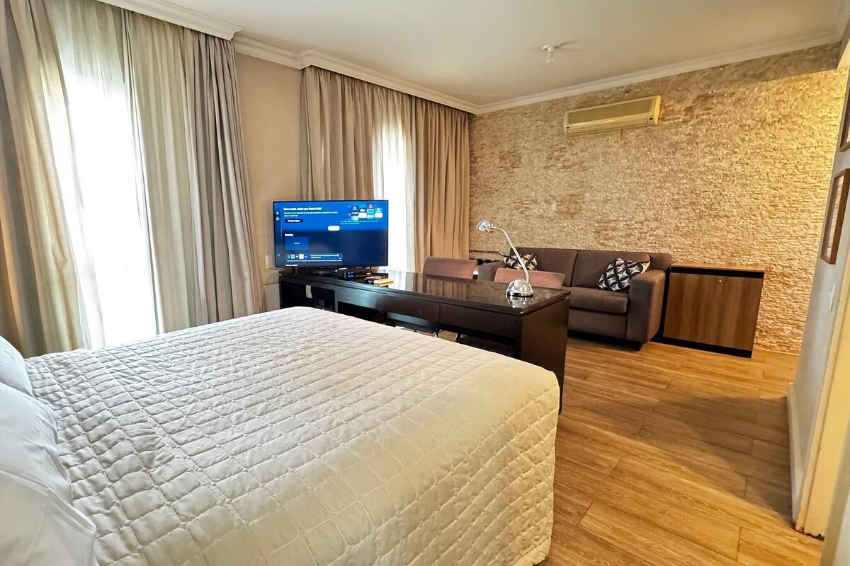 Een hotelkamer met een groot bed, een bureau met een computer, een bank en een wand met een stenen textuur.