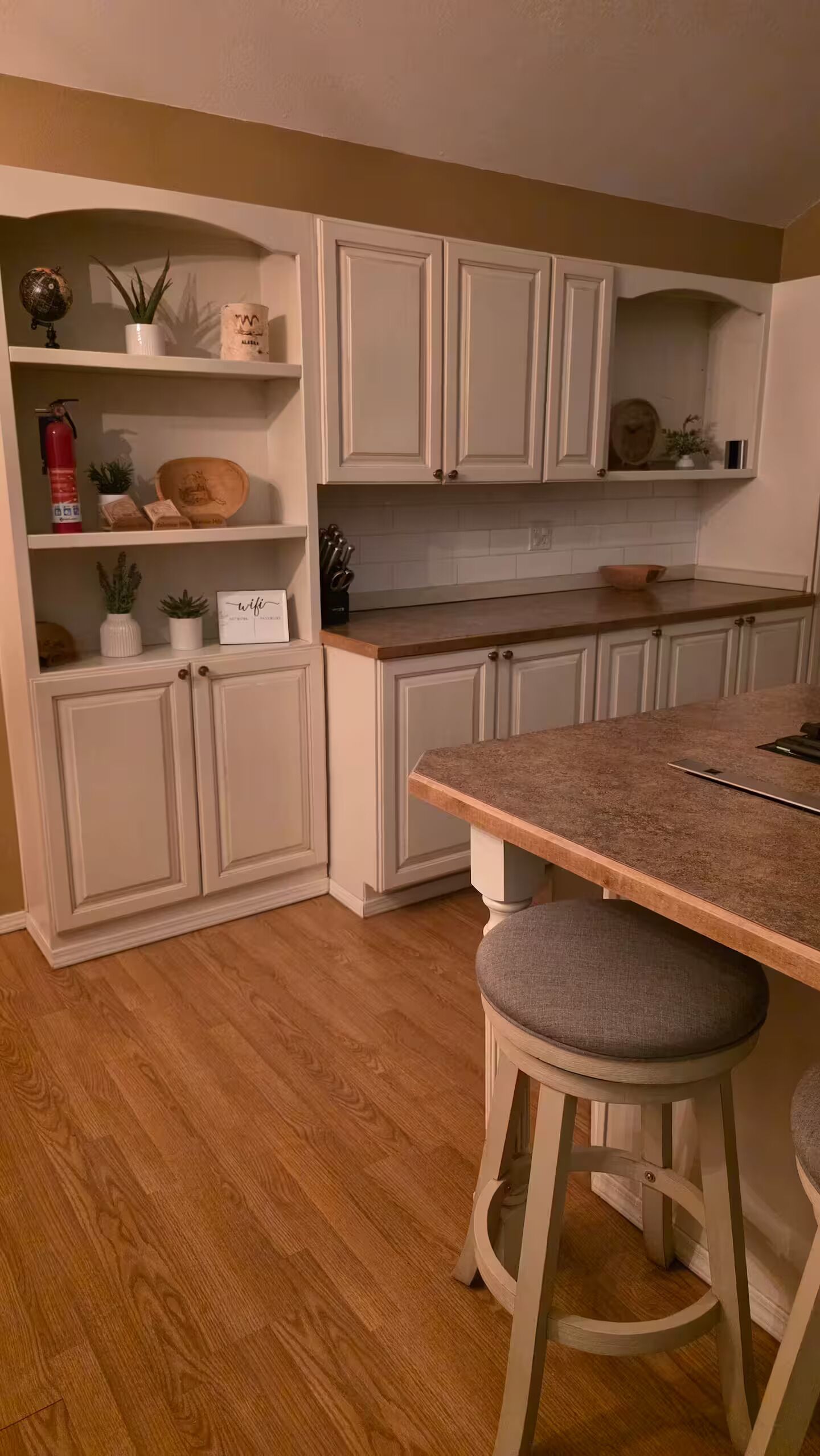 A kitchen with white cabinets, a wooden countertop, and a bar stool.