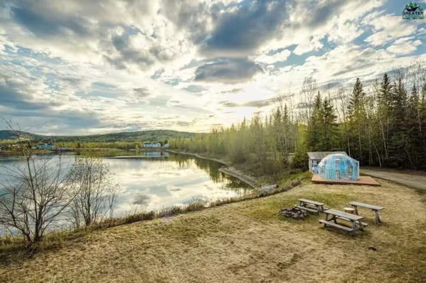 A lakeside cabin with a small dock, surrounded by trees and a picnic table.