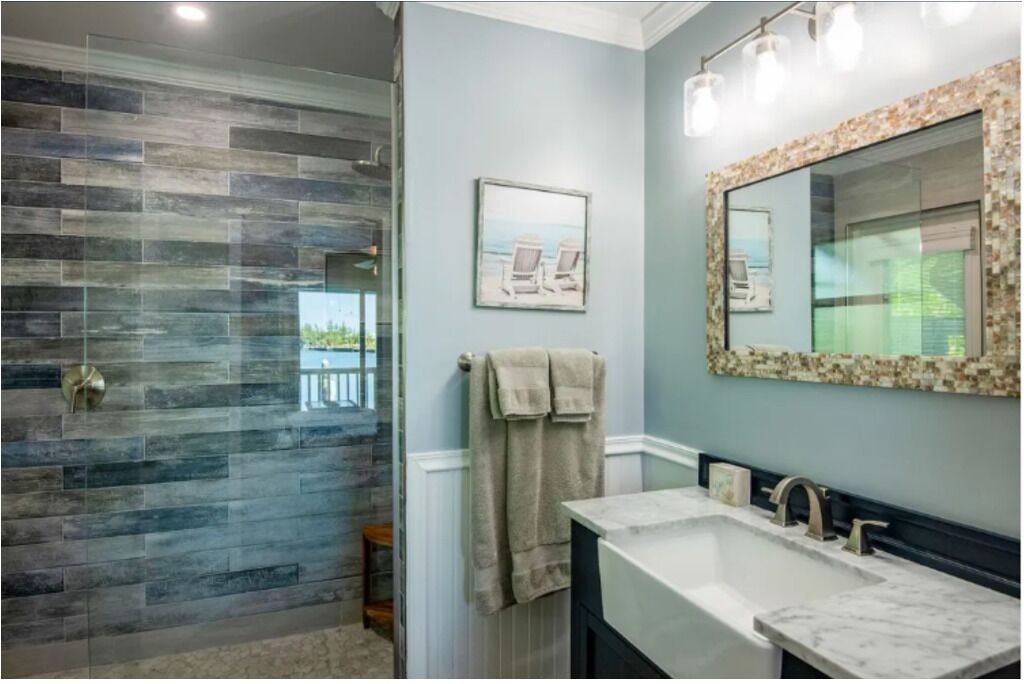 Une salle de bain avec une douche à parois de verre, un grand miroir avec un cadre décoratif et un porte-serviettes.