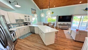 Una cocina moderna con armarios blancos, una isla central y un comedor con mesa y sillas.