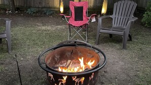 A backyard with a metal fire pit, two Adirondack chairs, and a red folding chair. - Woodland Beach House in lovely Tiny Beaches! (Elmvale)